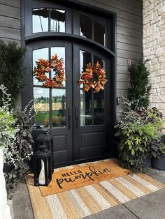 a black front door with two wreaths on the side and an entry mat that says happy thanksgiving