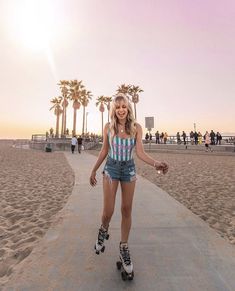 a woman riding roller skates on top of a sandy beach next to palm trees