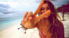 a woman making the v sign with her hand on an empty beach in front of the ocean