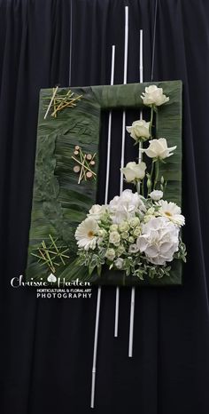 white flowers and greenery are arranged in a green rectangle on a black backdrop