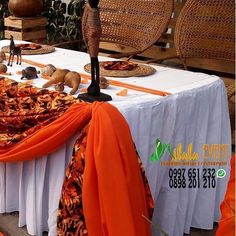 an orange and white table cloth draped over the top of a long table with food on it