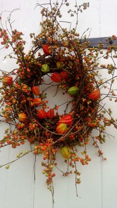 a wreath with red flowers and green leaves hanging from the side of a white door