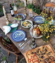 an outdoor table with plates and food on it, next to bottles of wine and candles