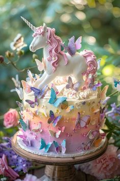 a cake decorated with butterflies and a unicorn figurine on top is sitting on a table surrounded by flowers