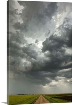 an empty dirt road in the middle of a field with storm clouds above and green grass on both sides