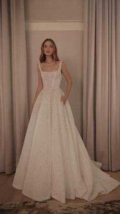 a woman standing in front of curtains wearing a wedding dress