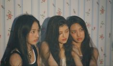 three young women sitting next to each other in front of a wallpapered background