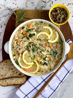 a bowl of soup with lemons, carrots and bread on a cutting board