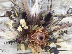 a vase filled with dried flowers and feathers on top of a wooden table next to a wall