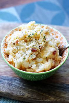 a green bowl filled with mashed potatoes on top of a wooden cutting board