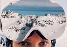 a woman wearing ski goggles with snow covered mountains in the background