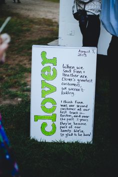 a sign that is in the grass with people standing around it and writing on it