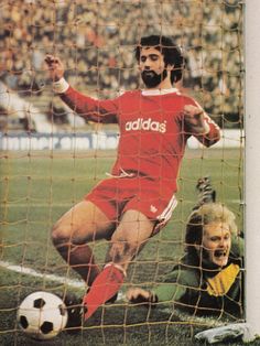 a man kicking a soccer ball in front of a net with an audience behind him