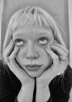 a black and white photo of a woman holding her hands to her face while looking at the camera