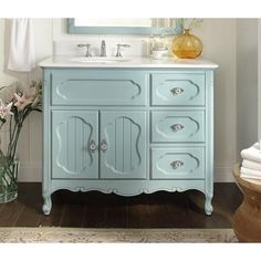 a bathroom vanity with blue painted drawers and white counter top, along with a vase filled with flowers