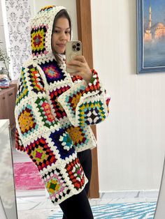 a woman taking a selfie in front of a mirror wearing a colorful crocheted sweater