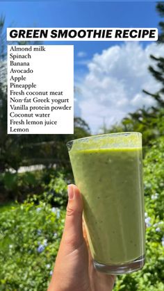 a hand holding up a green smoothie in front of some bushes and blue sky