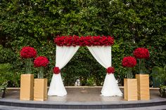 red flowers and white draping decorate this outdoor wedding ceremony area with gold boxes