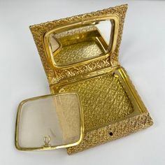 an open gold colored case with a mirror inside on a white tableclothed surface