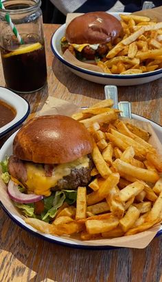 two plates with hamburgers and french fries are on the table next to some drinks