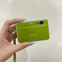 a person holding up a green camera in front of a white wall with feathers on it