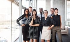 a group of business people posing for a photo in an office building, with their arms around each other