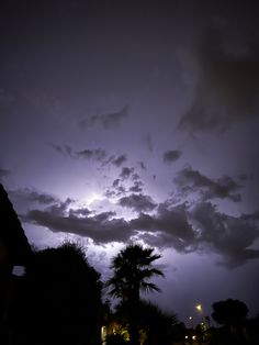 the sky is filled with dark clouds and bright lights in the distance are palm trees