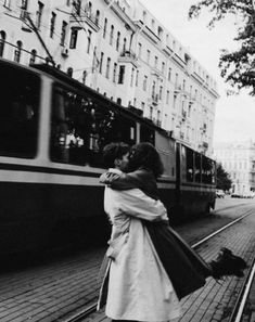 black and white photograph of two people hugging in front of a train