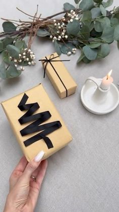 a person holding a small box with black ribbon on it next to some candles and flowers