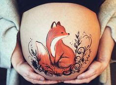 a pregnant woman holding her belly with a fox tattoo on it's side,