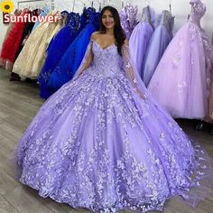 a woman is standing in front of dresses on display at a bridal shop, wearing a purple gown with floral appliques