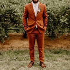 a man in an orange suit and tie standing in front of some trees with his hands in his pockets