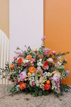 a bunch of flowers that are sitting on the ground in front of a yellow wall