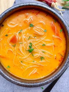 a bowl of soup with noodles and parsley on the side, next to a spoon