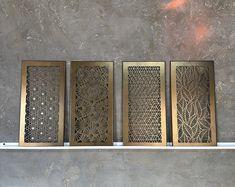 four decorative metal panels sitting on top of a white shelf next to a gray wall