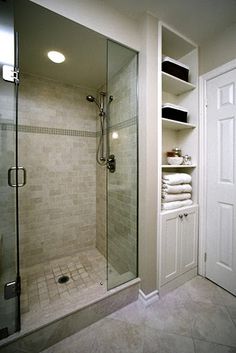 a walk in shower sitting inside of a bathroom next to a white closet filled with towels