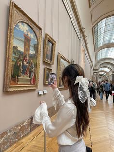 a woman taking a photo of paintings on the wall in a room with wooden floors