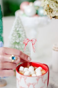 a person is pouring marshmallows into a red and white cup with a bow on it