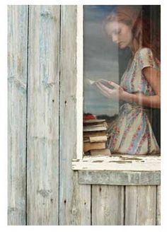 black and white photograph of a woman looking out the window with books in front of her