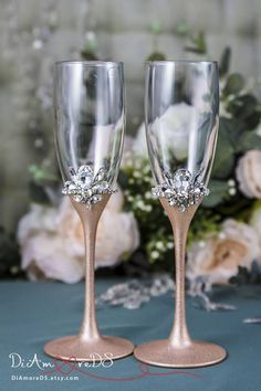 two champagne glasses sitting next to each other on a table with flowers in the background