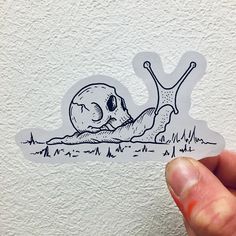 a hand holding up a sticker with a drawing of a snail crawling on the ground