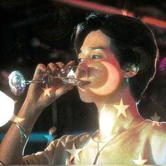 a woman drinking from a wine glass while wearing headphones and stars on her shirt