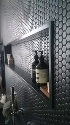 two bottles are sitting on the shelf above the sink in this black tiled bathroom area