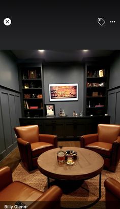 a living room with brown leather chairs and a round coffee table in front of a bookcase