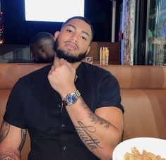 a man sitting at a table in front of a plate of food with his hand on his chin