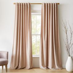 a living room with a chair and window covered in pink draping next to a plant