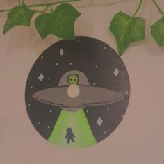 an alien flying through the air on top of a sticker next to green leaves