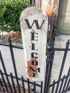 an old welcome sign is attached to a wrought iron fence with the word welcome painted on it