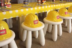 yellow hard hats are lined up on white stools in front of a long table