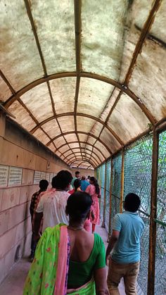 many people are walking down the walkway in an enclosed area with concrete walls and metal posts